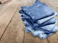 Pile di jeans su un tavolo di legno. Scopri come evitare che i jeans perdano colore.