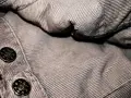 Dettaglio di un tessuto a coste marrone con bottoni metallici. Un invito a pulire le coste del tessuto per farle risaltare.