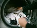Mani che caricano la lavatrice con panni chiari, sperando di non trovare macchie bianche sui vestiti dopo lavatrice.
