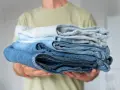 Un uomo tiene una pila di jeans duri dopo lavaggio, con tonalità di blu che vanno dal chiaro allo scuro.