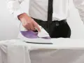 Uomo in camicia e cravatta stira una camicia bianca. L'immagine mostra l'uso di prodotti per stirare camicie, con il ferro da stiro in azione.