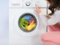 Donna preme il pulsante per avviare la lavatrice. Il cestello gira velocemente, mostrando i panni colorati in movimento.