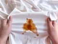 Mani che tengono un vestito bianco macchiato di caffè, forse caduto da una borsa in pelle.