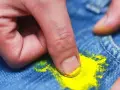 Dita che rimuovono macchia di vernice gialla dai jeans. Scopri come togliere tinta dai vestiti con metodi efficaci.