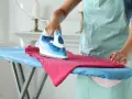 Donna stira una maglietta rosa con un ferro da stiro senza caldaia, il miglior ferro da stiro senza caldaia per risultati impeccabili.