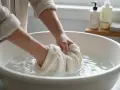Mani che lavano delicatamente un maglione di cashmere in una bacinella, facendo attenzione che il cashmere si restringe se trattato male.