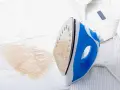 Un ferro da stiro blu e bianco lascia una macchia giallastra su una camicia bianca a righe sottili.