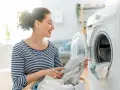 Donna sorridente carica la lavatrice con panni, inclusi tessuti sintetici.