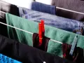 Panni stesi su uno stendibiancheria, con mollette rosse e azzurre. Un modo semplice per capire come strizzare i panni a mano.