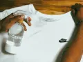 Mano che spruzza una maglia bianca con una soluzione antimacchia. Ecco come smacchiare una maglia bianca.