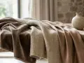 Tessuti morbidi e drappeggiati su un tavolo di legno. Il velluto è cotone, con una texture liscia e calda, accanto a un tessuto più grezzo e una seta lucida.