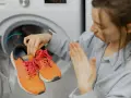 Donna con scarpe arancioni davanti a una lavatrice. Scopri come fare un lavaggio a vuoto per pulire la lavatrice.