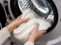 Mani che inseriscono un maglione bianco nella lavatrice, sperando che la lavatrice non lava bene i bianchi.