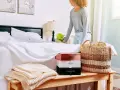 Donna sistema il letto con lenzuola bianche. Sul comodino, scatole di profumi e coperte. Scopri come ammorbidire il cotone nuovo.