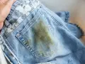 Jeans macchiati in lavatrice, con una grossa macchia verde-marrone sul retro.