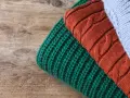 Close-up of folded knitted wool in green, rust, and light blue on a wooden surface.