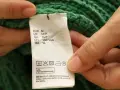Etichetta di un maglione verde che indica il lavaggio in lavatrice a 30 gradi, con istruzioni per il lavaggio del cotone.
