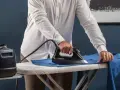 Uomo stira una camicia blu su un asse da stiro. Impara come stirare il poliestere con cura per risultati impeccabili.