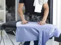 Uomo stira camicia azzurra con vapore. Per un lavaggio misto in lavatrice, quanti gradi?