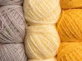 Gomitoli di lana in tonalità naturali: grigio, giallo tenue e giallo vivace. Diversi tipi di lana pronti per creare maglie calde.