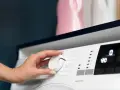 Mano che gira la manopola della lavatrice per impostare la temperatura. A quanti gradi si lavano i colorati? Forse 30° o 40°.