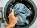 Mano inserisce jeans nella lavatrice. Scopri come lavare i jeans in lavatrice per mantenerli come nuovi.