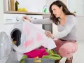 Donna sorpresa scopre una maglietta bianca macchiata di rosa, tipici errori di bucato causati dalla dispersione del colore.