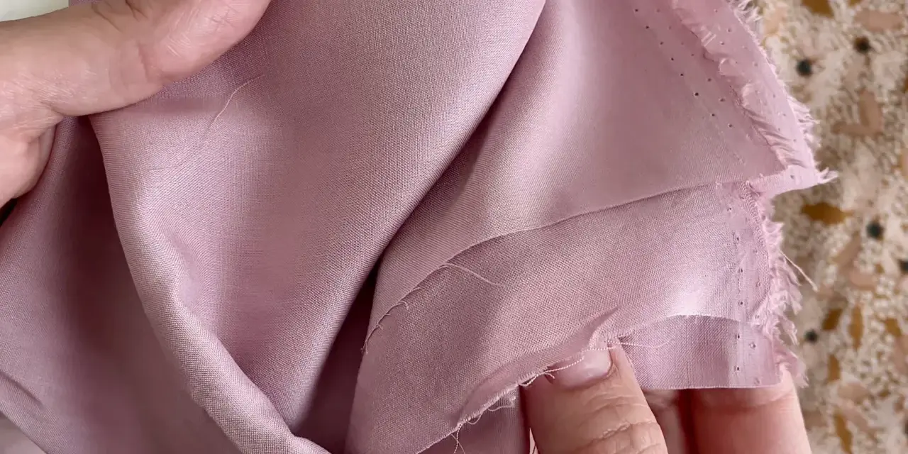 Mani che accarezzano un tessuto di viscosa rosa cipria, mostrando come lavare la viscosa a mano per preservarne la morbidezza.