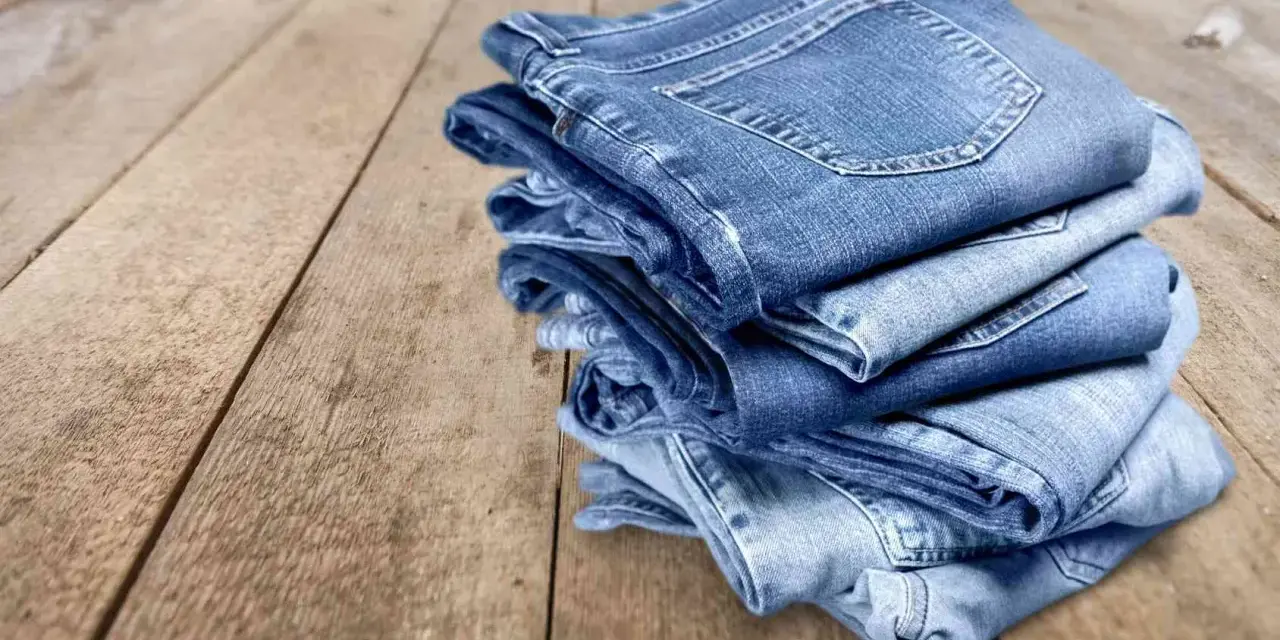 Pile di jeans su un tavolo di legno. Scopri come evitare che i jeans perdano colore.