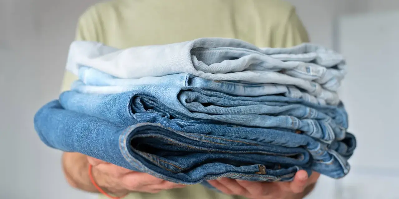 Un uomo tiene una pila di jeans duri dopo lavaggio, con tonalità di blu che vanno dal chiaro allo scuro.