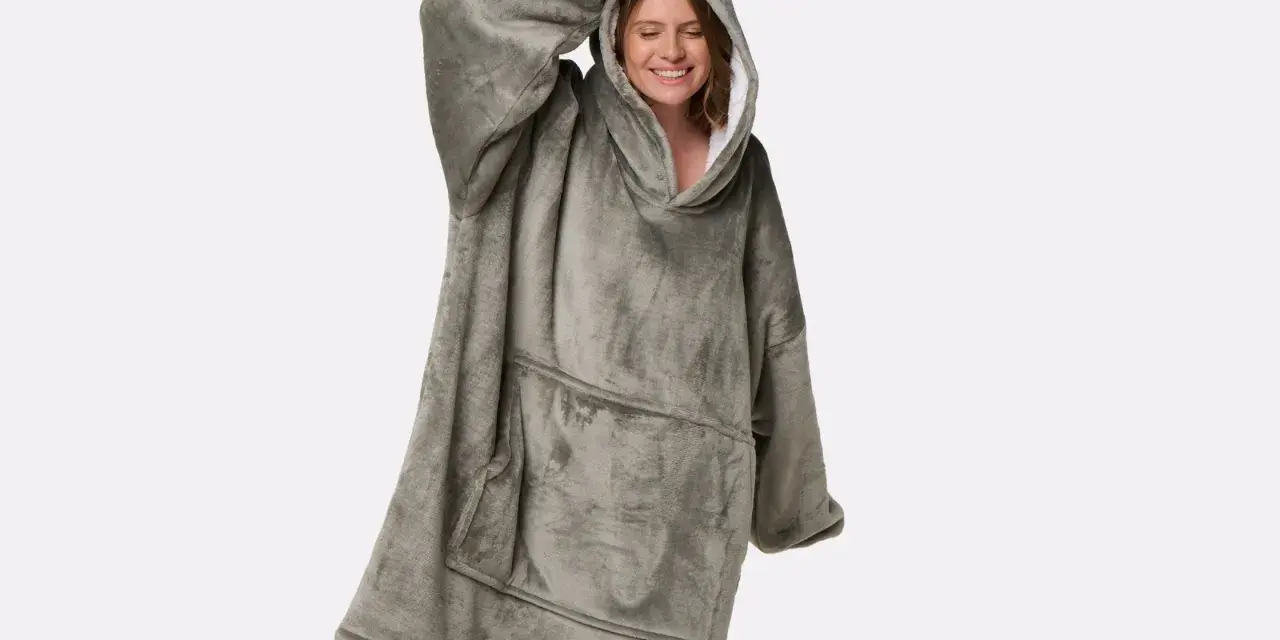 Donna sorridente indossa una coperta con cappuccio grigia, realizzata in poliestere, un materiale sintetico caldo e confortevole.