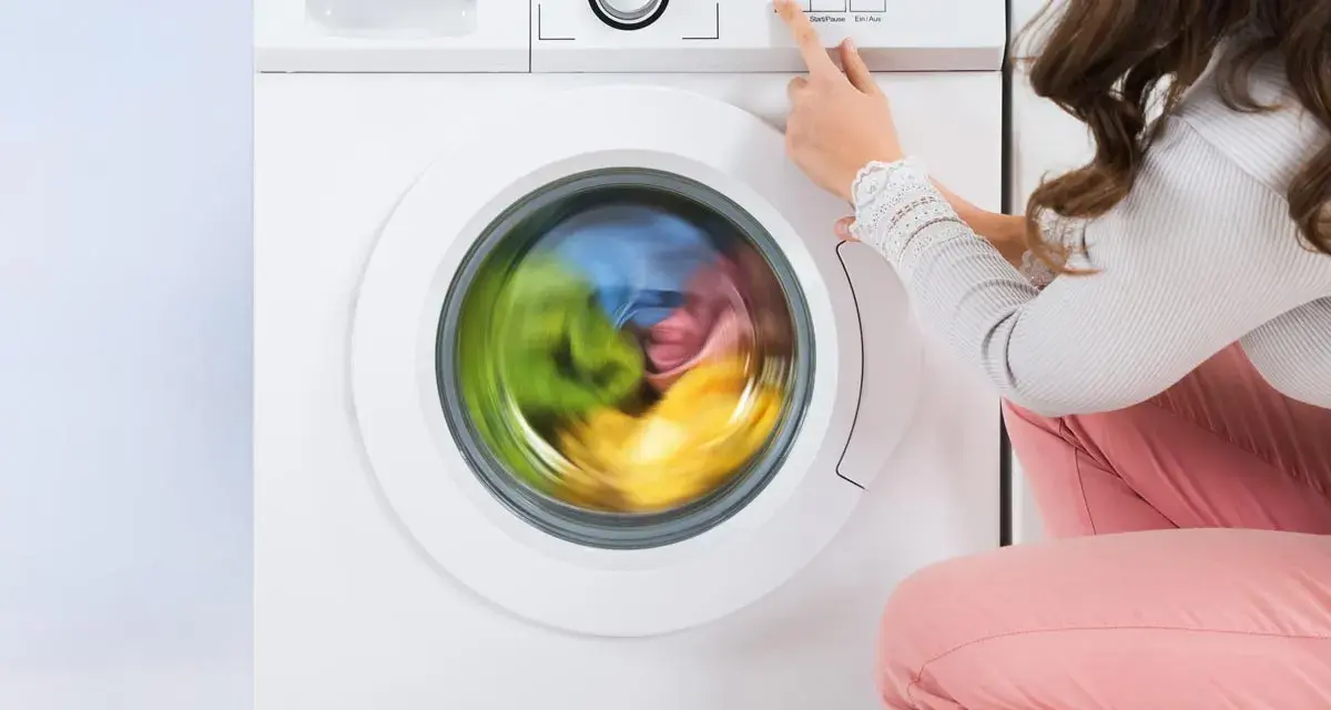 Donna preme il pulsante per avviare la lavatrice. Il cestello gira velocemente, mostrando i panni colorati in movimento.