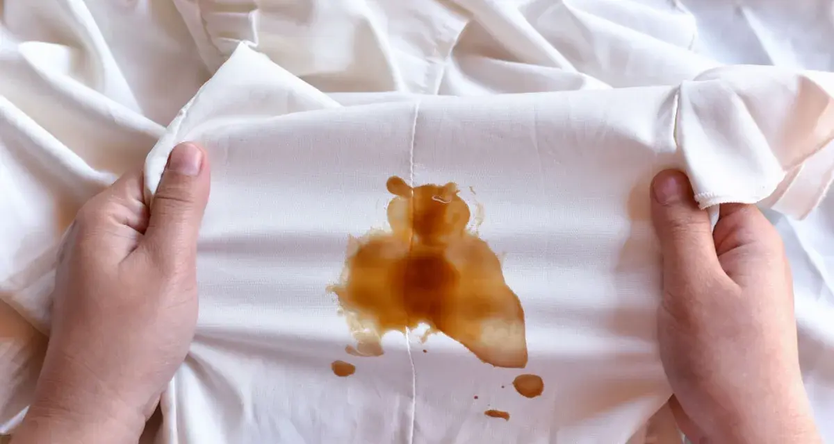 Mani che tengono un vestito bianco macchiato di caffè, forse caduto da una borsa in pelle.