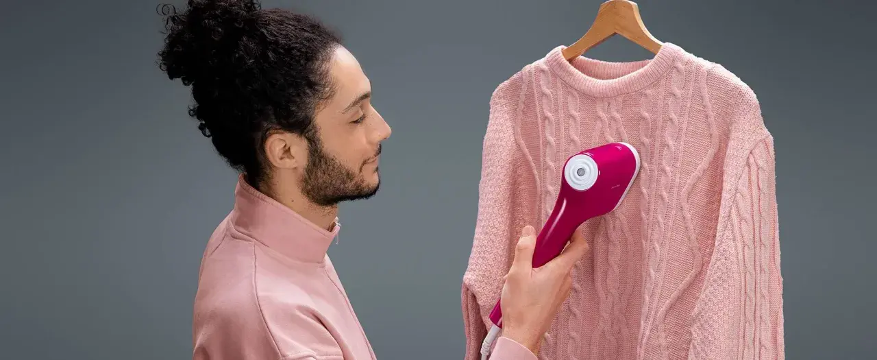 Uomo con maglione rosa usa un ferro da stiro verticale che non emette vapore, sperando di eliminare le pieghe.