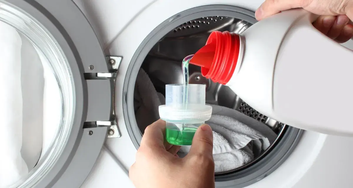 Versando detersivo liquido in un misurino per il prelavaggio lavatrice.