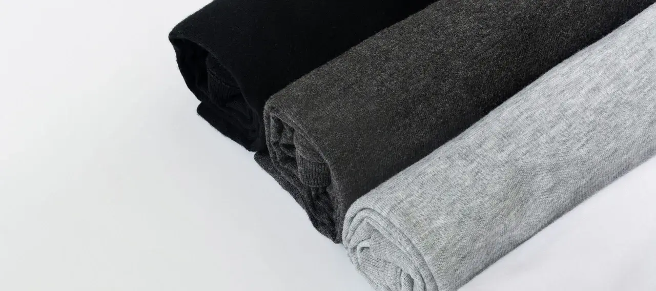 Come lavare un capo bianco e nero in lavatrice: tessuti arrotolati in nero, grigio scuro e grigio chiaro.