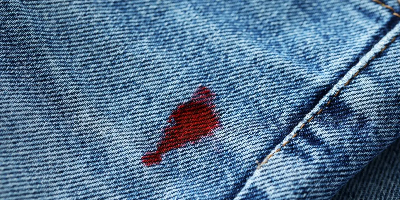 Macchia rossa su jeans blu. Attenzione, l'acqua ossigenata macchia i vestiti, lasciando segni indelebili.