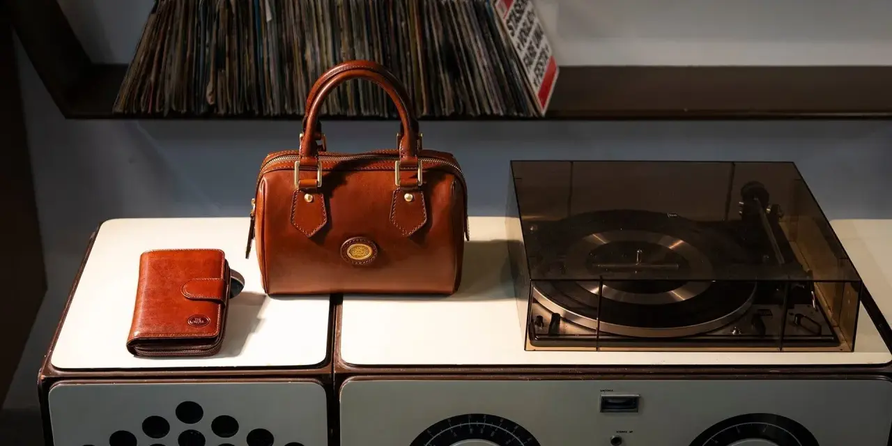 Borsa in pelle marrone, portafoglio e giradischi vintage. Un set per chi ama la musica e lo stile classico, pronto per essere pulito.