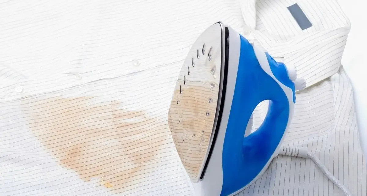Un ferro da stiro blu e bianco lascia una macchia giallastra su una camicia bianca a righe sottili.