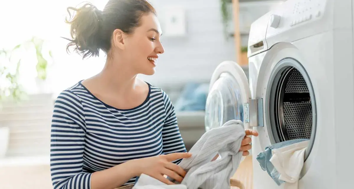 Donna sorridente carica la lavatrice con panni, inclusi tessuti sintetici.