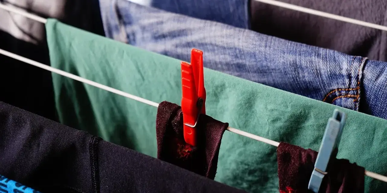 Panni stesi su uno stendibiancheria, con mollette rosse e azzurre. Un modo semplice per capire come strizzare i panni a mano.