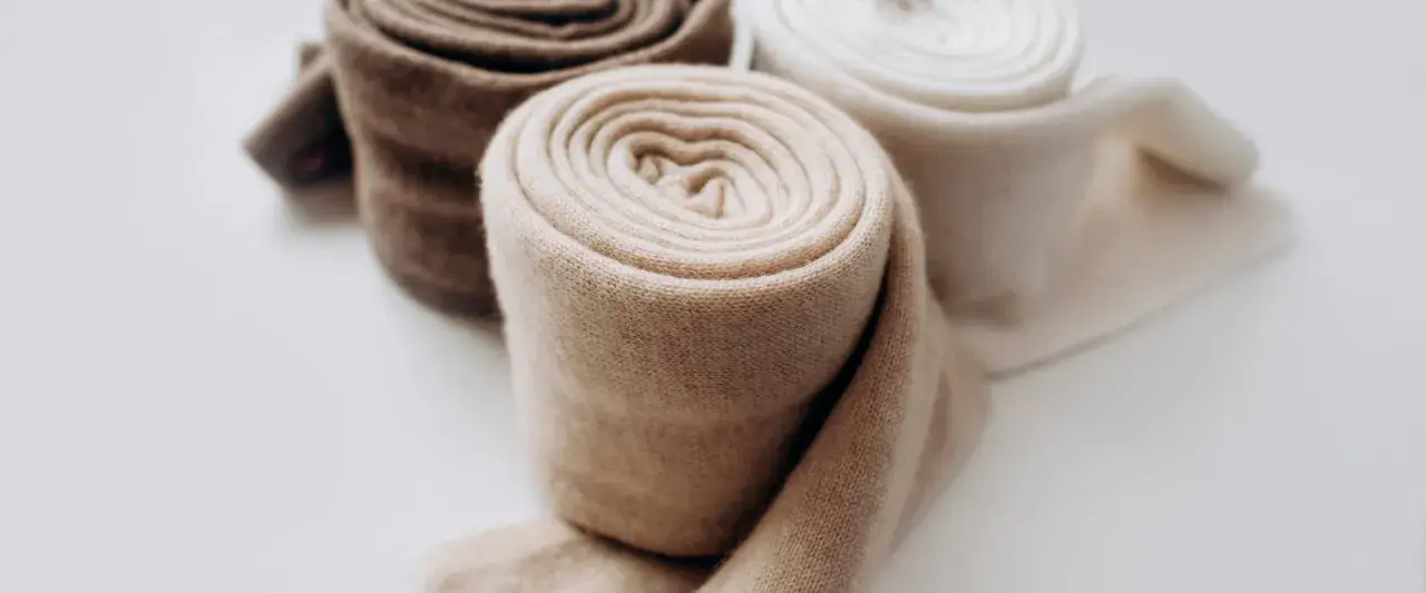 Rotoli di morbido cashmere in tonalità naturali, pronti per il lavaggio e la cura.