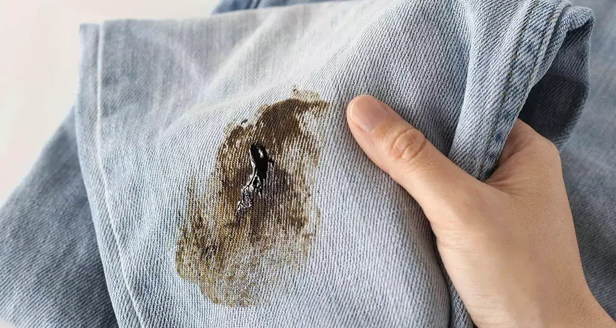 Mano che mostra un jeans macchiato, pronto per essere smacchiato.