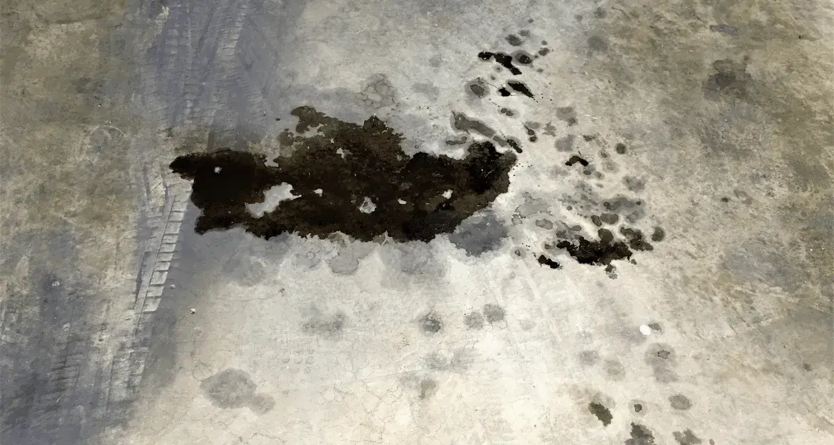 Macchie scure di grasso meccanico su cemento, con impronte di pneumatici. Un problema comune da risolvere per chi vuole togliere macchie di grasso meccanico.