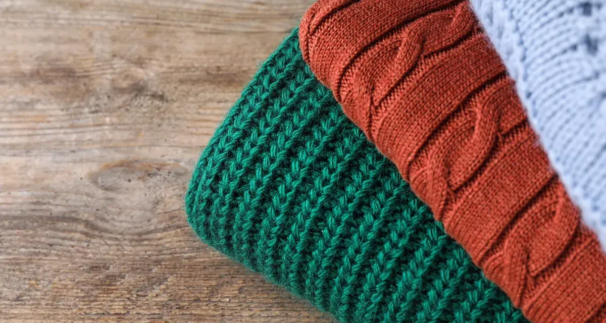 Close-up of folded knitted wool in green, rust, and light blue on a wooden surface.