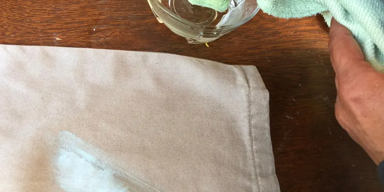 Mani che tamponano macchie di colore su tessuto con un panno umido.