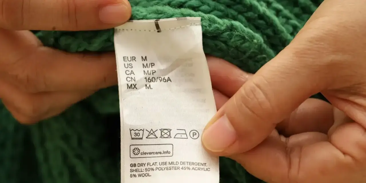 Etichetta di un maglione verde che indica il lavaggio in lavatrice a 30 gradi, con istruzioni per il lavaggio del cotone.