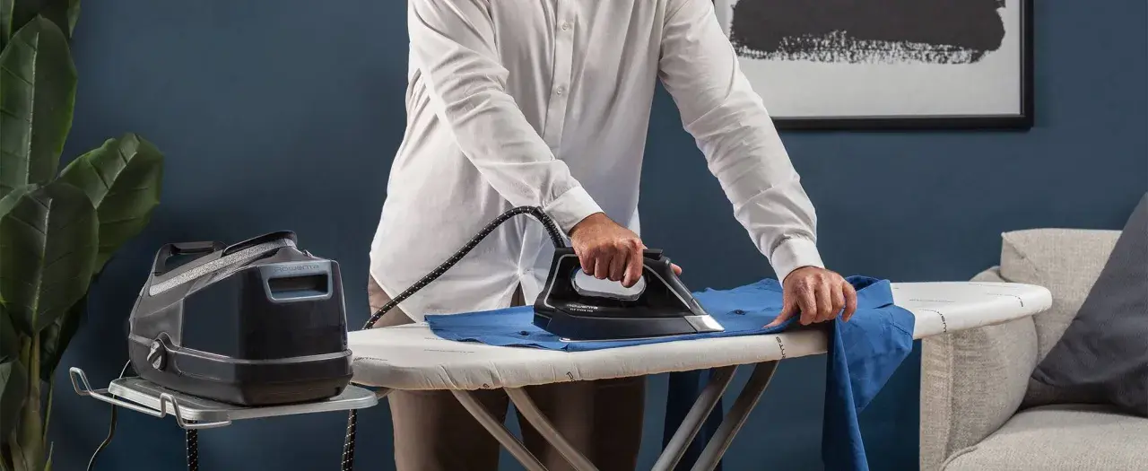 Uomo stira una camicia blu su un asse da stiro. Impara come stirare il poliestere con cura per risultati impeccabili.