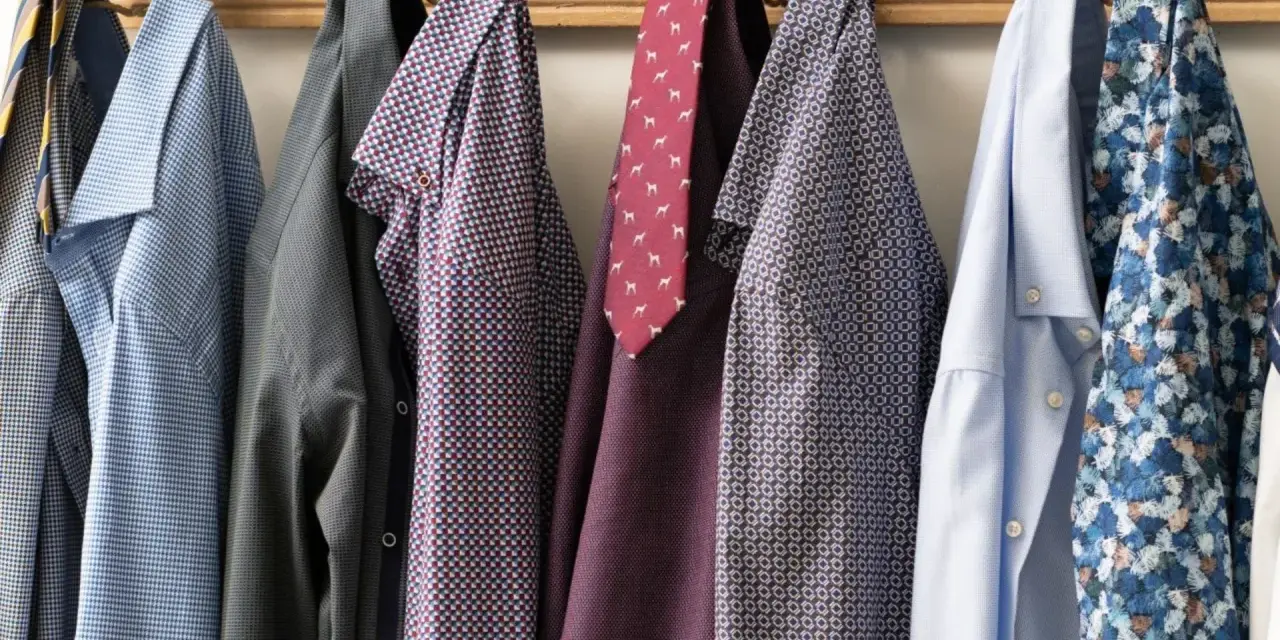 Camicie da uomo con fantasie diverse appese a un attaccapanni. Un promemoria su come lavare le camicie a mano per mantenerle perfette.