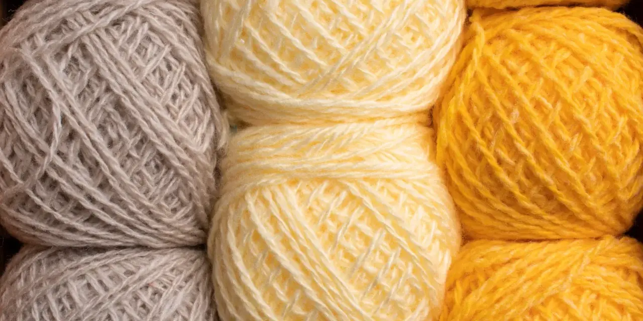 Gomitoli di lana in tonalità naturali: grigio, giallo tenue e giallo vivace. Diversi tipi di lana pronti per creare maglie calde.